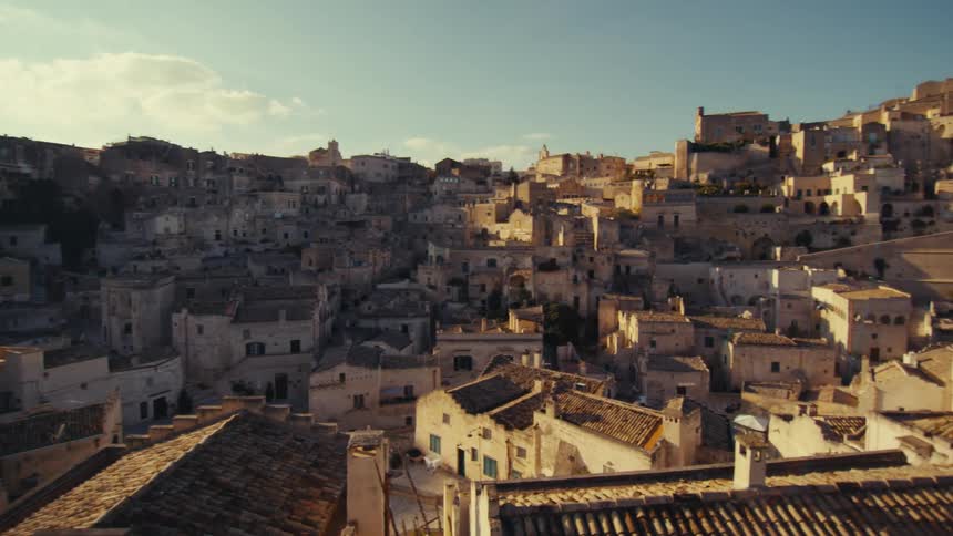 A hand pointing towards a breathtaking panoramic view of a historic town nestled on a hillside with numerous buildings constructed directly into the rock face bathed in the warm glow of the setting sun