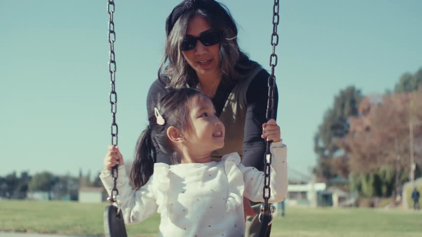 Mother pushing young child on a chain link swing at a park