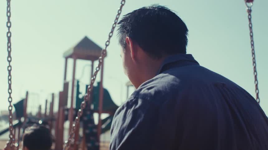 A father pushes his toddler son on a swing in a park playground on a sunny day