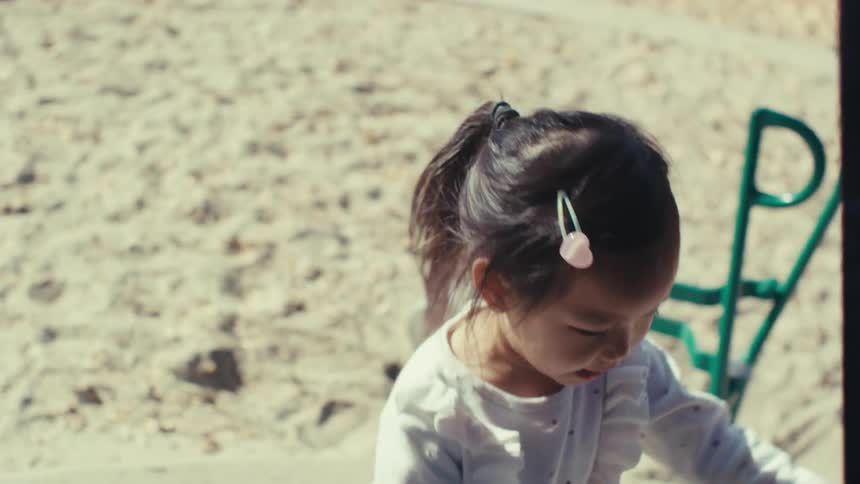 Girl playing in the sand of a playground next to an adult