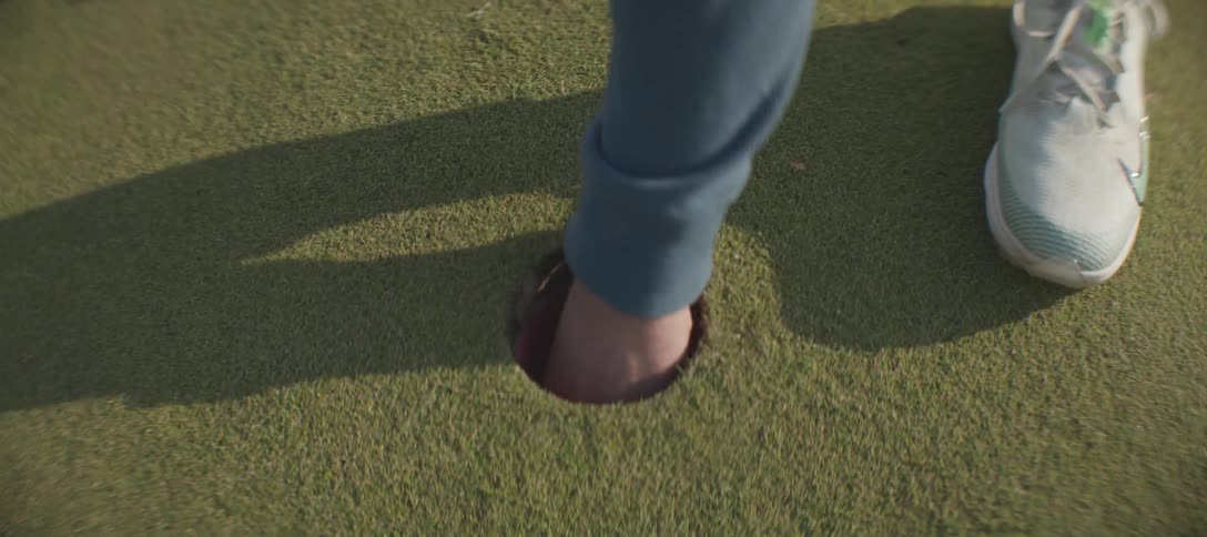A golfer sinks a putt and picks up the ball from the hole