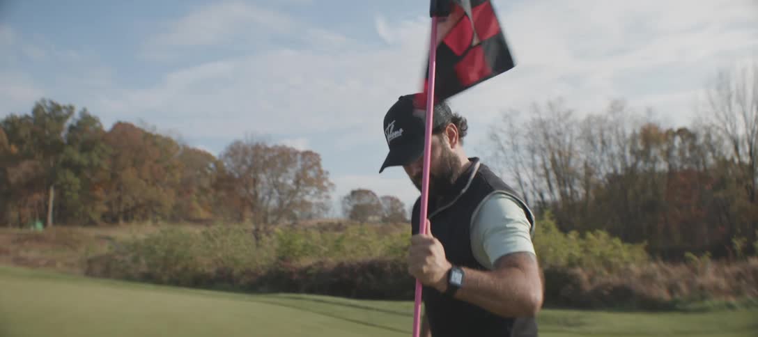 A man holding a golf flag on a wellmaintained golf course