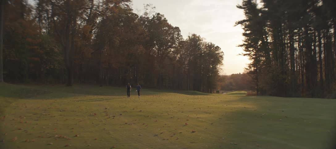Two golfers walking along a fairway on a golf course as the sun sets casting long shadows across the green grass