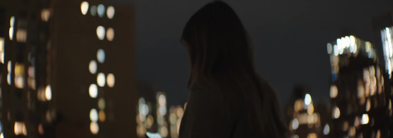 Woman walking on a terrace at night interacting with a smartphone