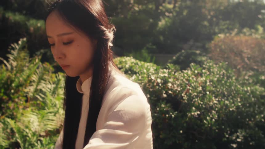 A woman is playing a guzheng a traditional chinese string instrument in a sunlit lush garden