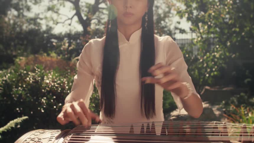 Woman sitting in a garden playing a stringed musical instrument