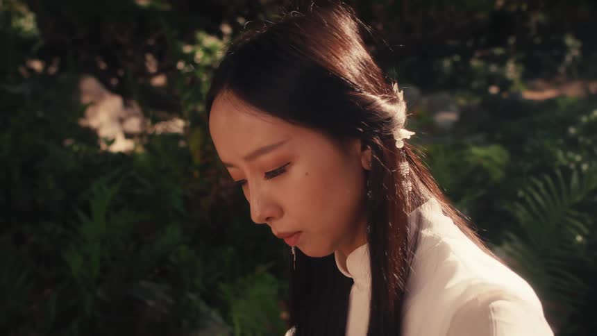 A woman dressed in traditional attire playing a guzheng a chinese stringed instrument outdoors in a serene sunlit garden