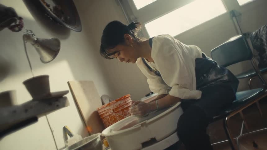 Woman sitting in front of a machine producing a clay vase