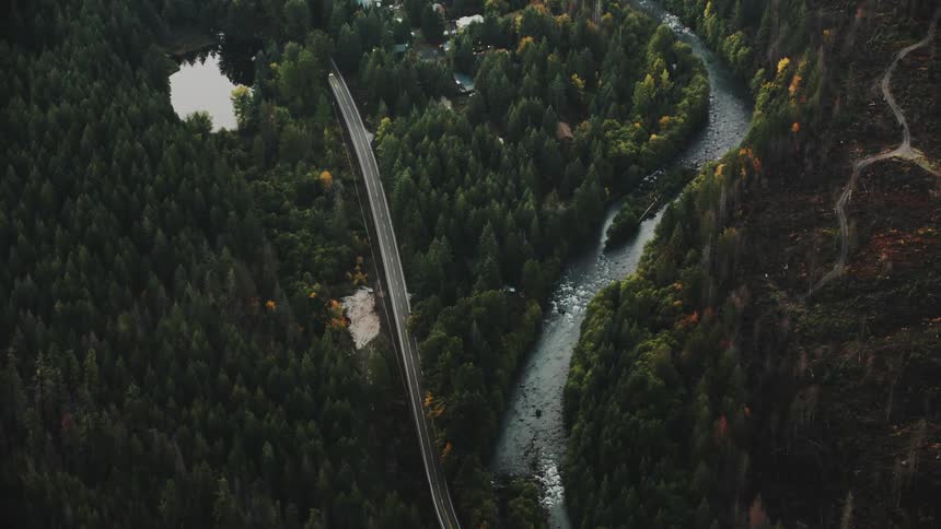An aerial view of a winding river flowing through a lush green valley with a road paralleling its course and a small lake nestled amongst the trees