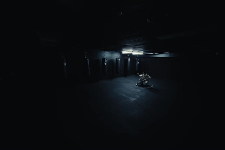 A martial arts athlete crouches on the dimly lit gym floor wrapping her hands with white bands