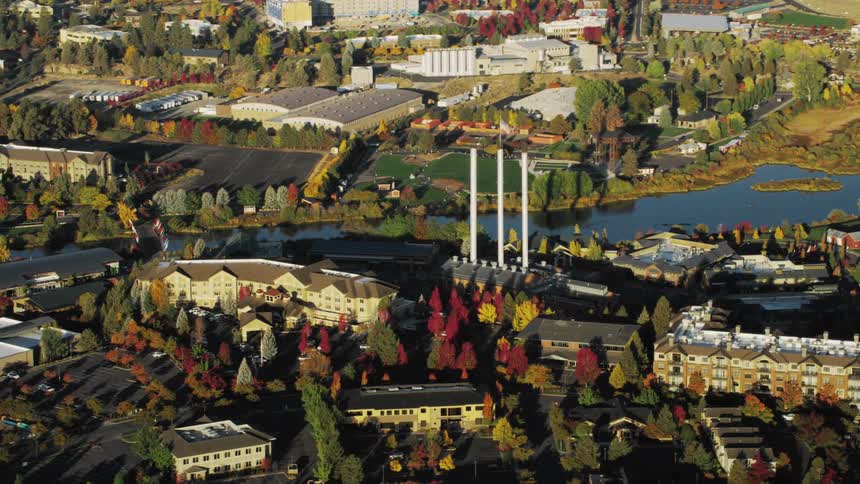 An aerial view of bend oregon featuring a river park autumn trees and the distinctive smokestacks of the old mill district