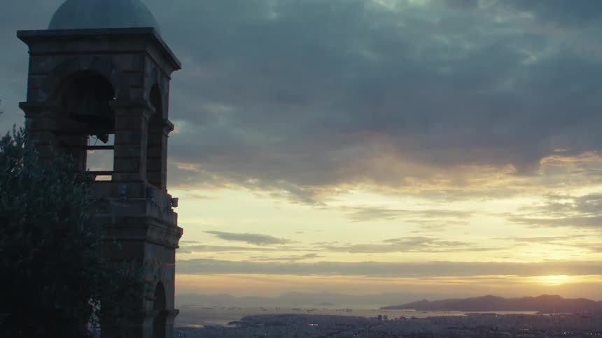 A dramatic sunset over a sprawling city with the silhouette of a bell tower standing tall against the vibrant sky
