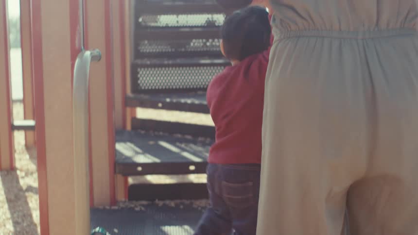 Mother holding hands with her little son climbing a toy in an outdoor playground