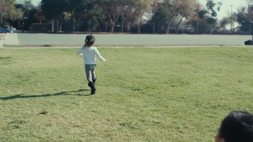 Father putting his little daughter down as she runs across the grass next to his other son