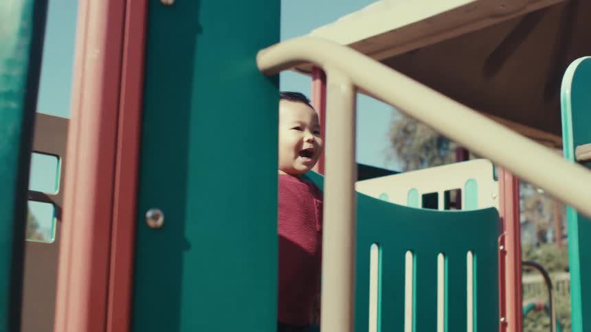 A happy child climbs on a playground with a slide in a park on a sunny day