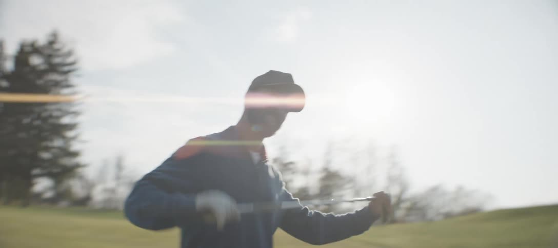 Man in cap holding golf club walking through a field happily