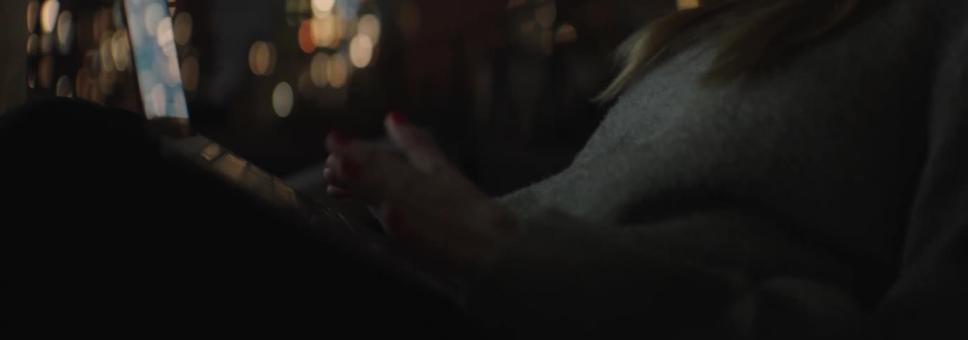 Woman typing on a laptop that is on her legs in an outdoor location at night