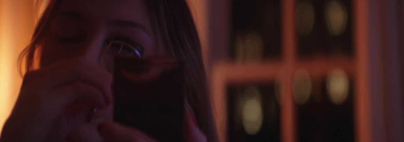 A woman curling their eyelashes with an eyelash curler illuminated by warm and dim light