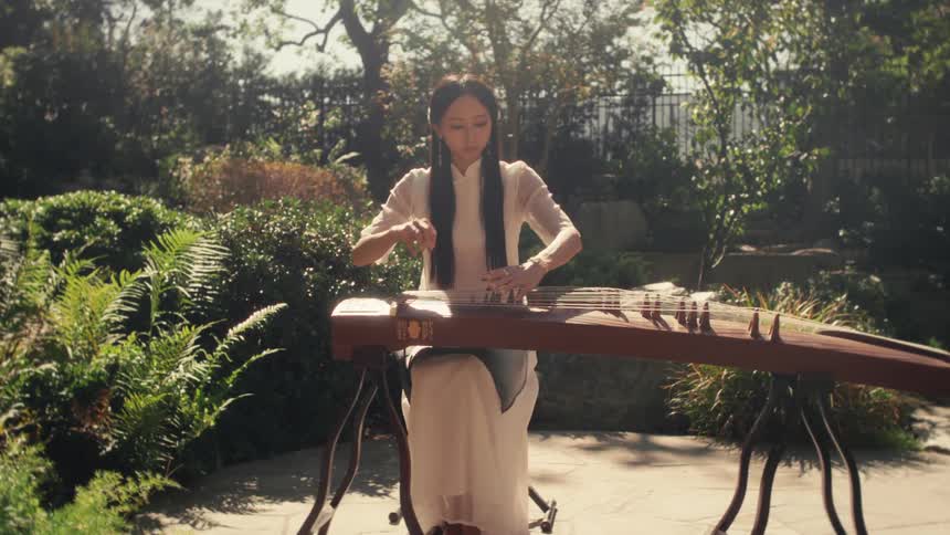 A woman is playing a guzheng a traditional chinese string instrument in a sunlit lush garden
