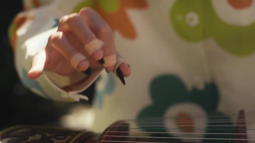 A woman wearing a colorful shirt with a floral pattern playing a guzheng a traditional chinese plucked string instrument