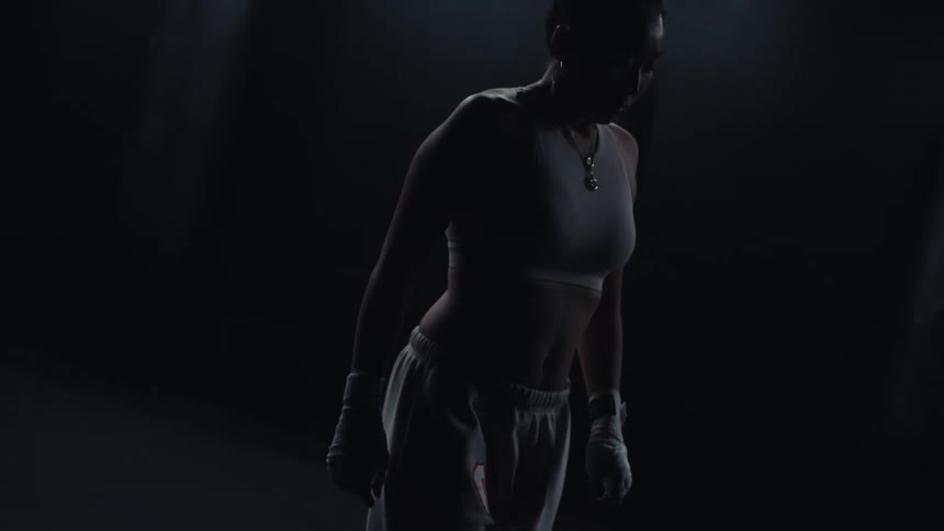 A woman walks in the dark gym towards the heavy bags