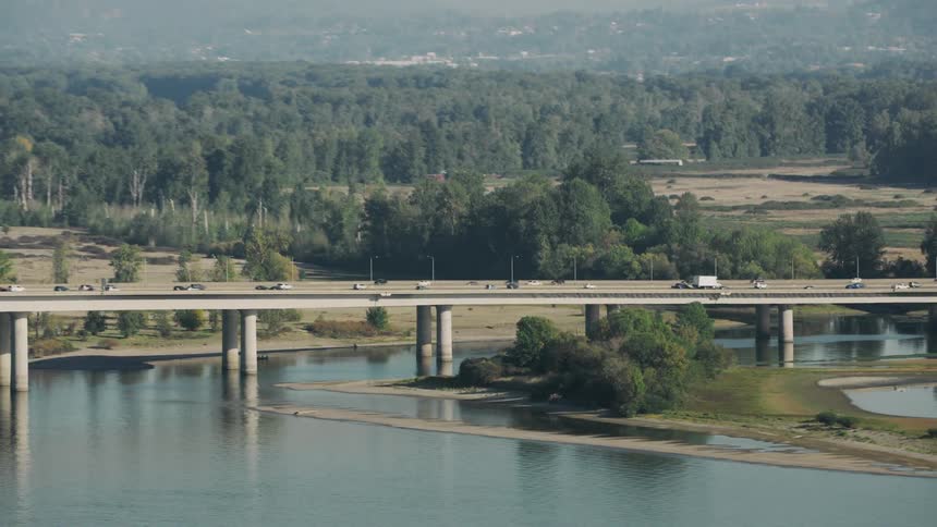 Aerial view of a viaduct above a lake with vehicle traffic and forest in the background