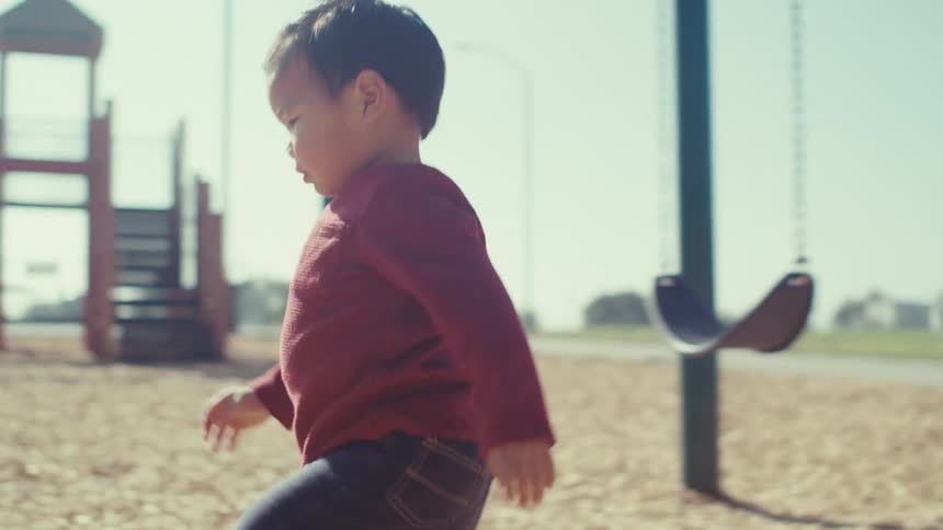 Little boy getting off swing at playground next to his mother