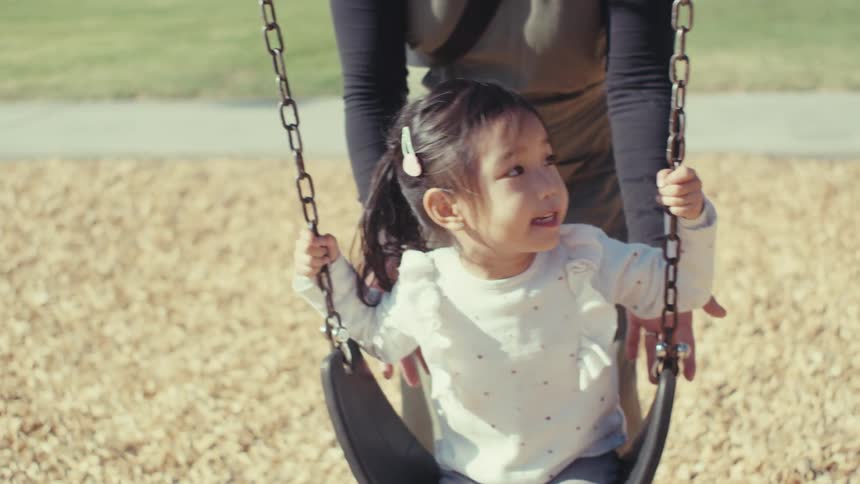 Mother pushing her little daughter on a swing outdoors