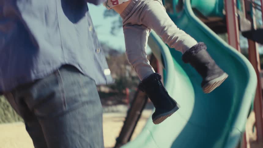 A father picks up his daughter who just slid down a slide in a parks play area