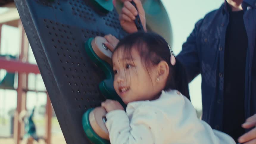 Girl with help from father climbing and playing on an outdoor toy