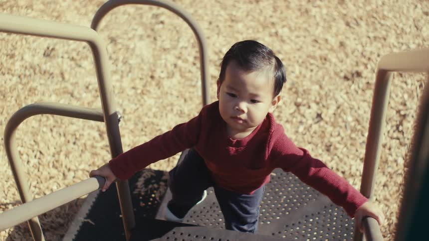 A child slowly climbs the stairs in the playground