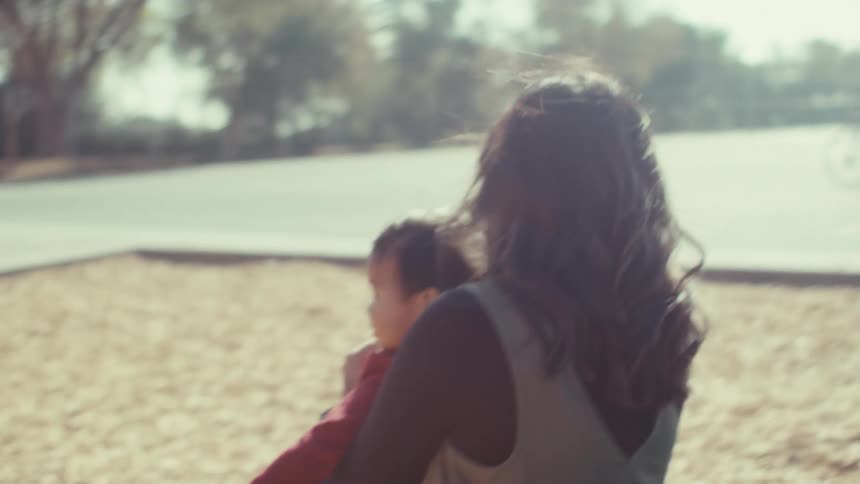 Mother with her little son on her lap going down the slide at the playground together