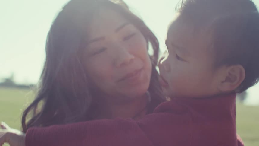 A mother holds her toddler son outside and hugs him as he points to something