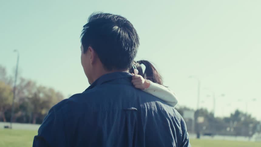 Father and mother carry their kids while walking across the grass at the park on a sunny day