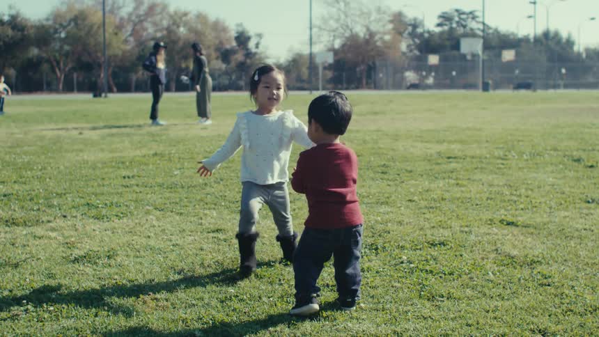 Father in a park with his two young children and they walk through a field happily