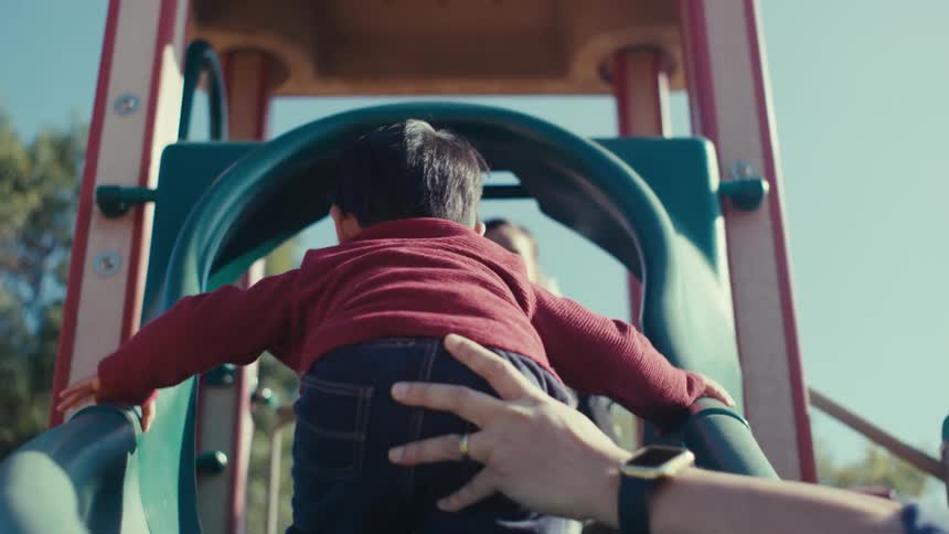 Parents help their children climb a playground in a park on a sunny day
