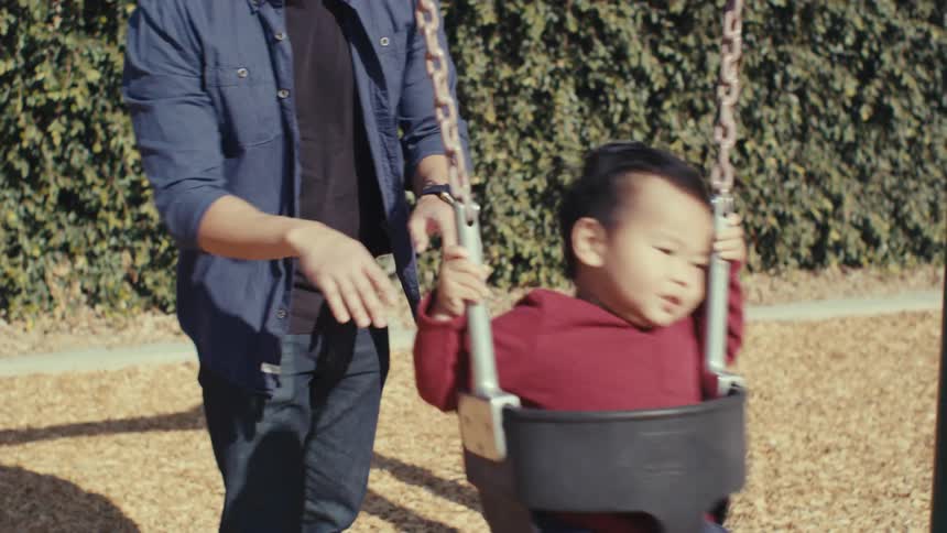A father pushes his toddler on a bucket swing at a playground