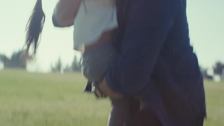 A father raises his daughter in his arms and they share a kiss in a park on a sunny day