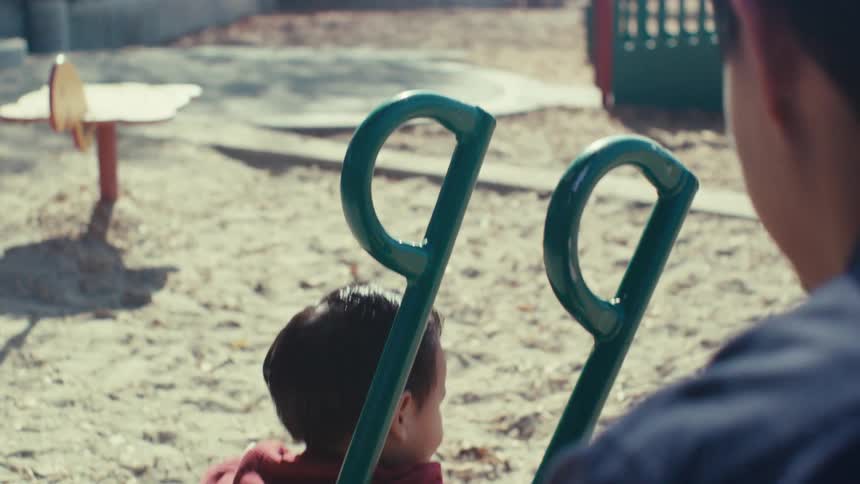 Father next to his son who is playing in the sand at a playground