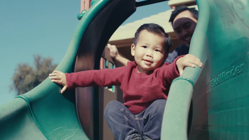 Father accompanying his young son on an outdoor playground toy during the day