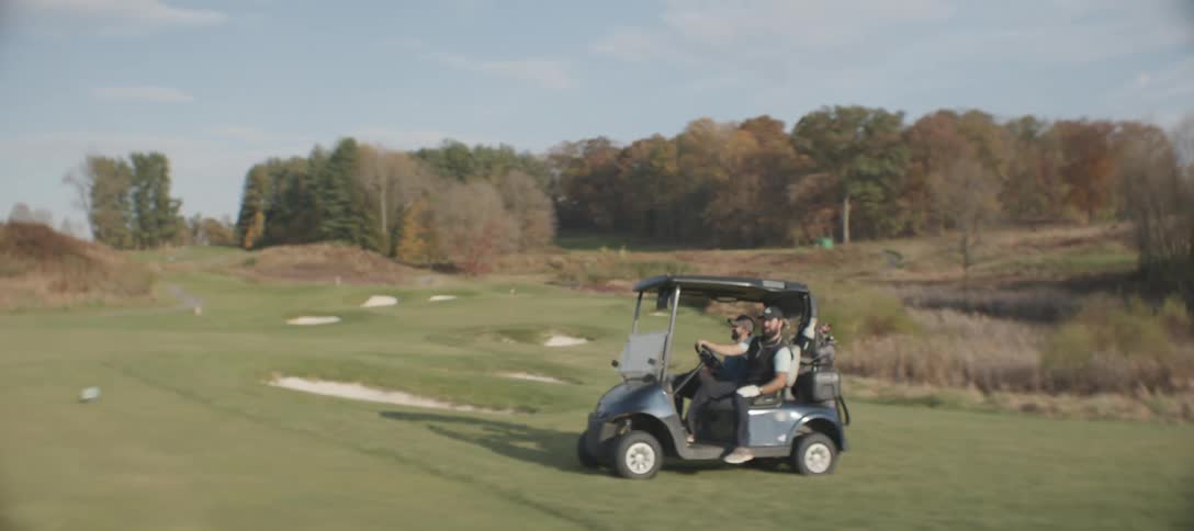 Two men riding in a golf cart through a field