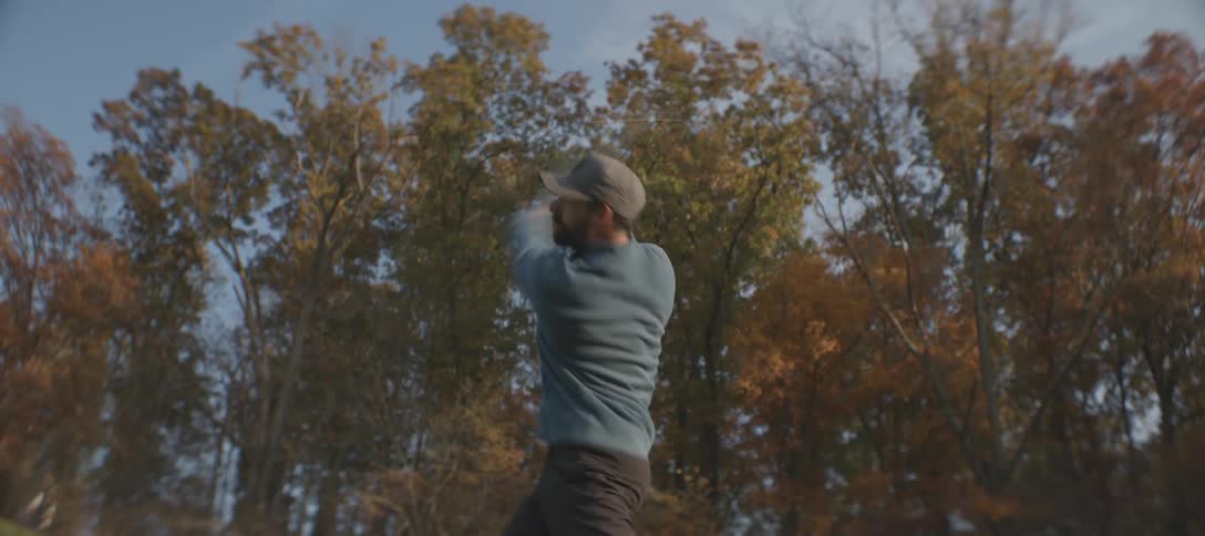 A bearded male is swinging a golf club outdoors