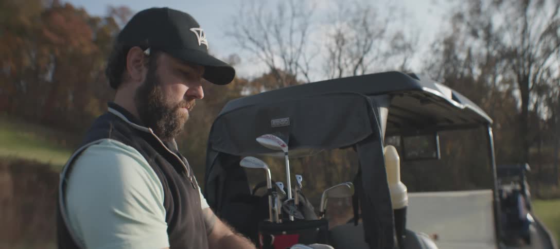 A male golfer grabs a club from a golf bag on an autumn day