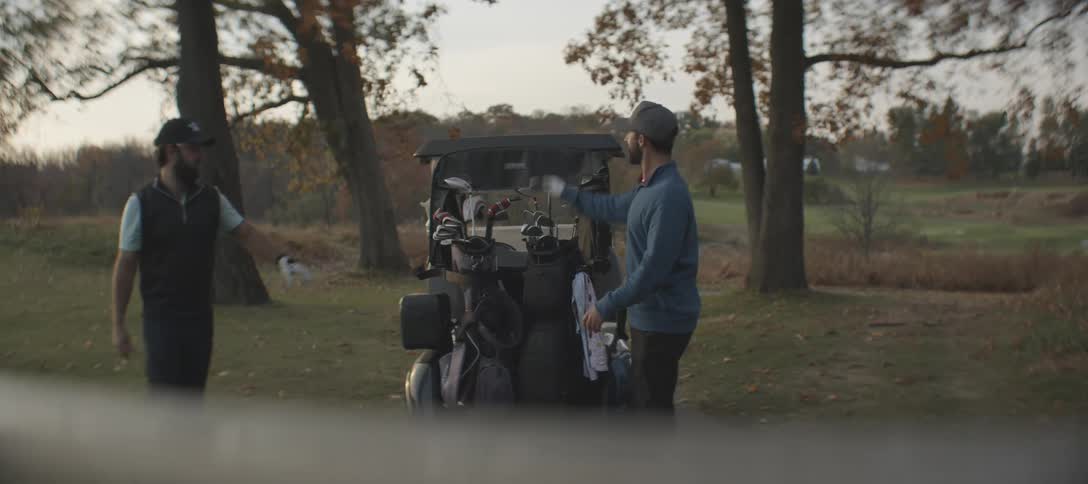 Two male golfers getting out of golf cart and grabbing thier golf clubs