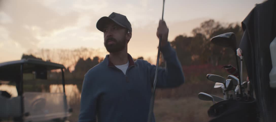 Man in a natural field picking up a golf club