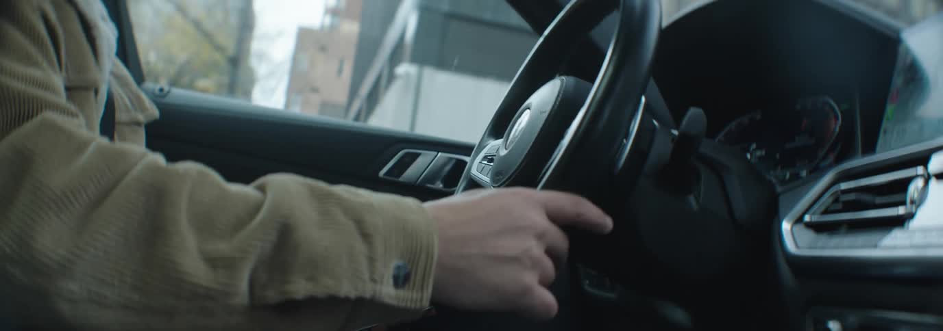 A man with a brown corduroy jacket driving a car their hand gripping the steering wheel