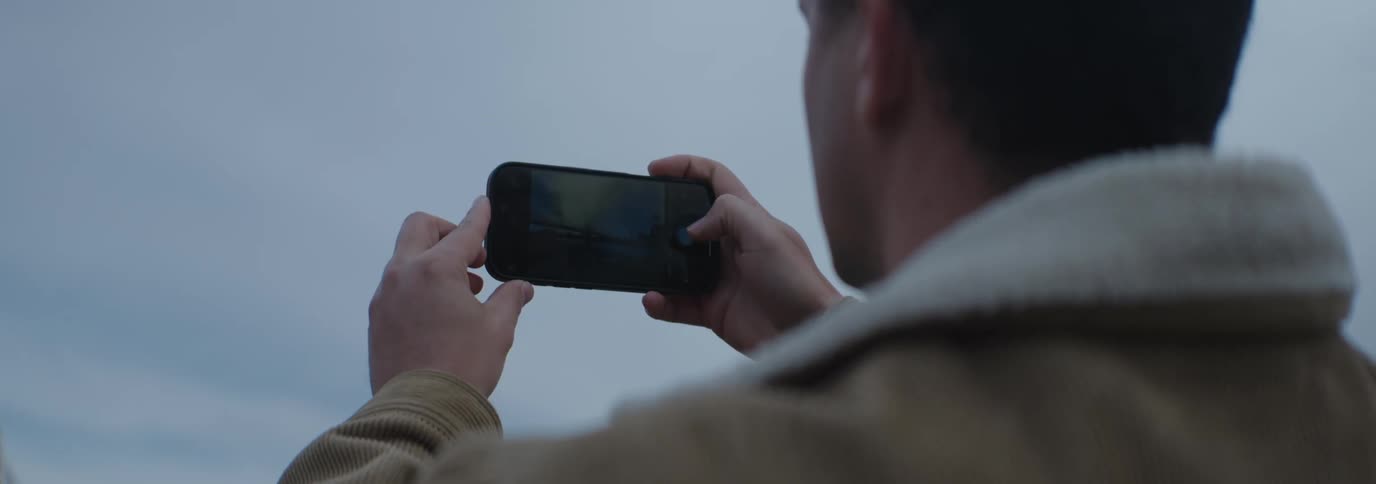 Man turning his cell phone sideways and taking a picture outdoors