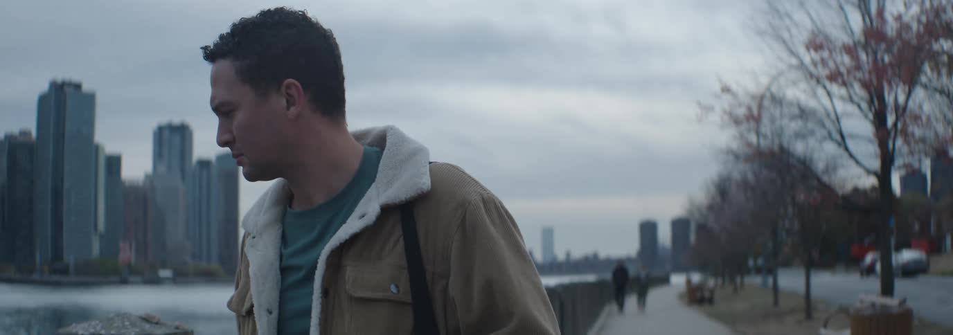A man walks by the water near the big city