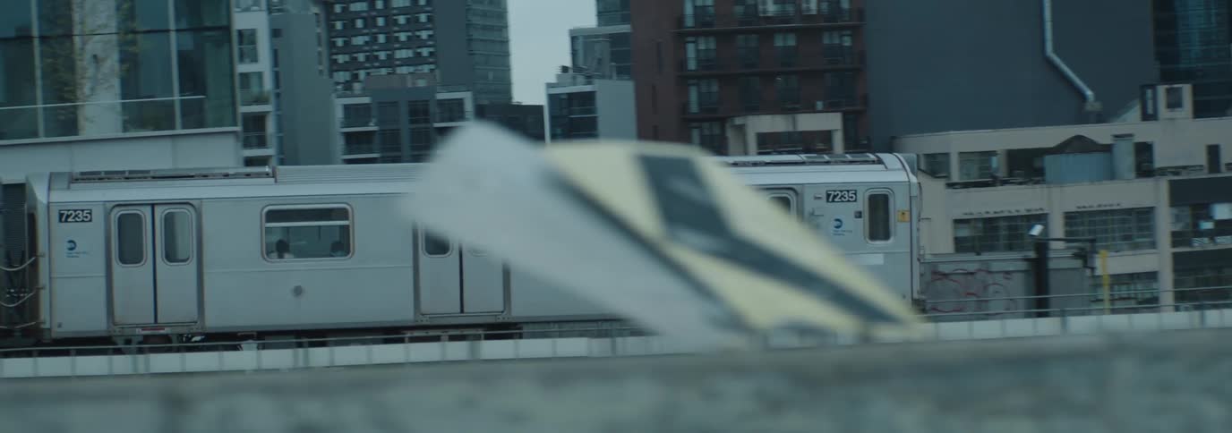 A white subway train traveling through a city with tall buildings in the background