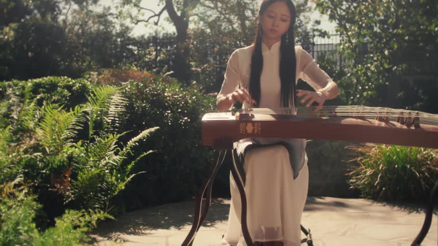 A woman dressed in traditional attire playing a guzheng a chinese stringed instrument outdoors in a serene sunlit garden